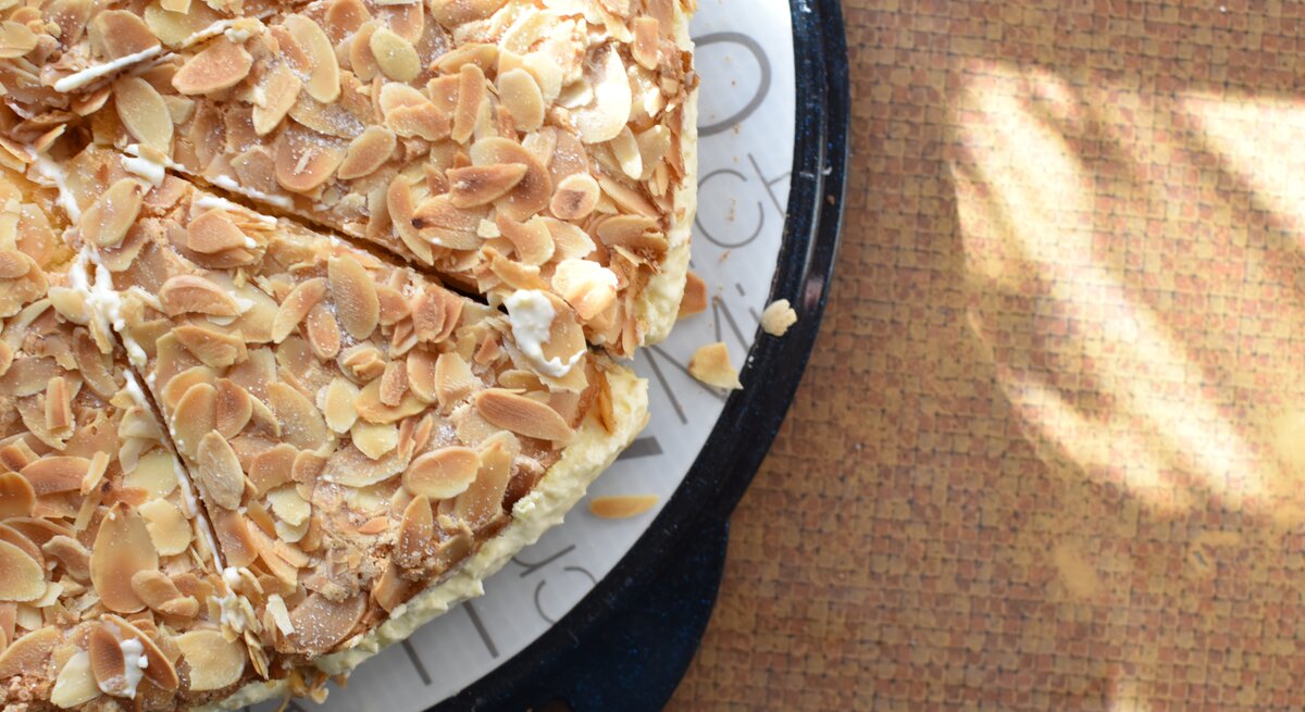 Bienenstich ohne Hefe auf Kuchenplatte auf braunem Untergrund. Alles nah und direkt von oben fotografiert.