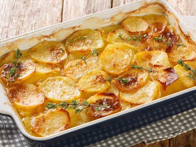 Französische Bäckerinkartoffeln in weißer Auflaufform auf Holz. | © Getty Images/ALLEKO