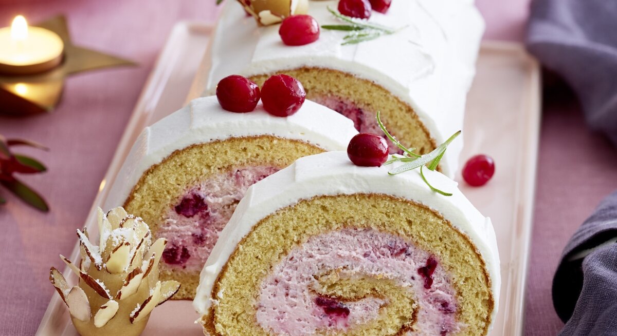 Auf einem Teller liegt eine  Marzipan-Cranberryrolle. Sie ist mit frischen Beeren und Marzipan verziert.