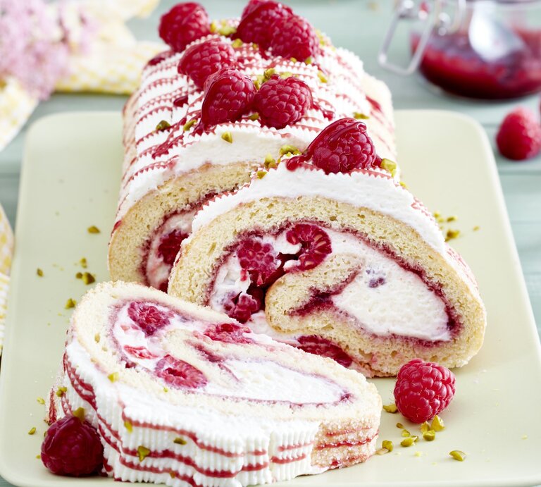 Eine sahnige Himbeerrolle mit Schmand liegt auf einer rechteckigen Porzellanplatte. Drumherum liegen Himbeeren und Servietten. | © EAT CLUB / Isabell Triemer