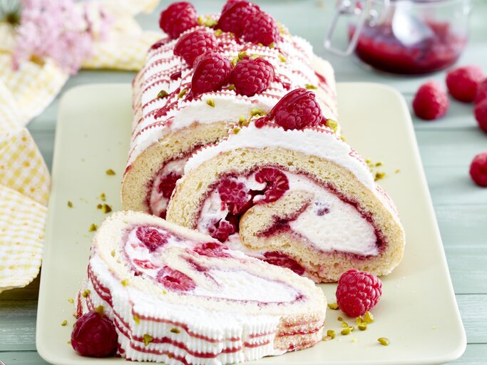 Eine sahnige Himbeerrolle mit Schmand liegt auf einer rechteckigen Porzellanplatte. Drumherum liegen Himbeeren und Servietten. | © EAT CLUB / Isabell Triemer