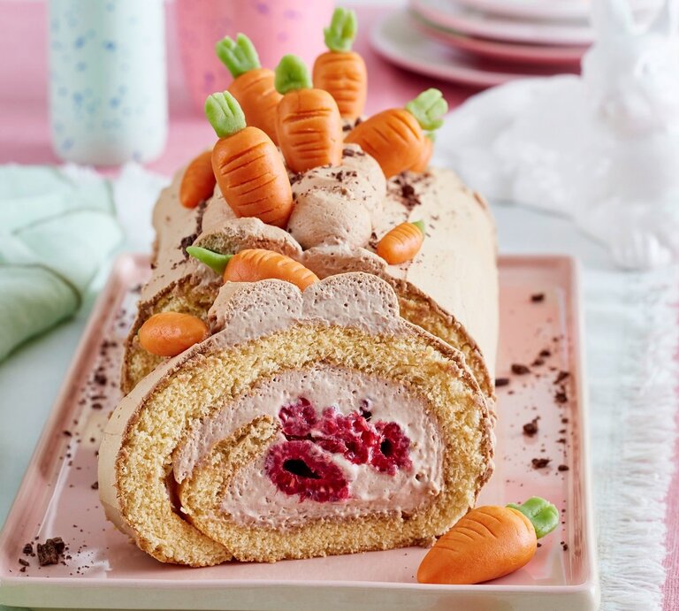 Auf einer Kuchenplatte ist eine Möhren-Biskuitrolle serviert. Sie ist mit Möhren aus Marzipan dekoriert.  | © EAT CLUB / Isabell Triemer