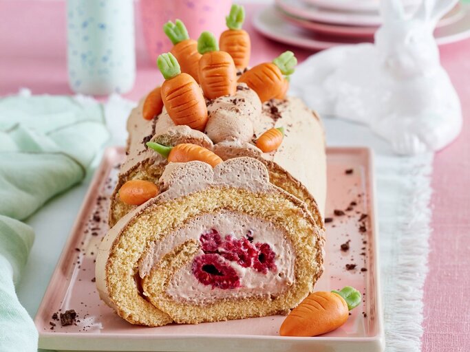Auf einer Kuchenplatte ist eine Möhren-Biskuitrolle serviert. Sie ist mit Möhren aus Marzipan dekoriert.  | © EAT CLUB / Isabell Triemer