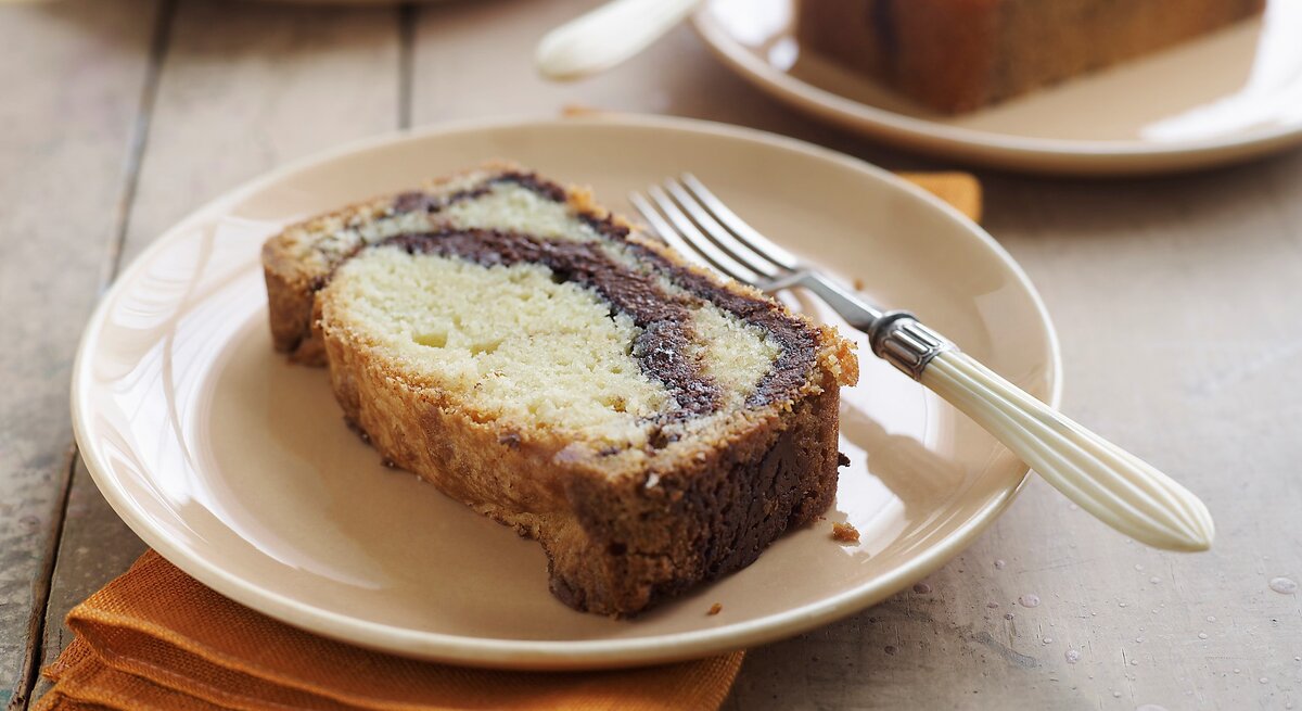 Ein heller Tisch mit mehreren weißen Tellern auf dem jeweils ein Stück Marmorkuchen mit Nutella liegt. Am Rand des Tellers eine Gabel mit weißem Griff und darunter eine gelbe Serviette.