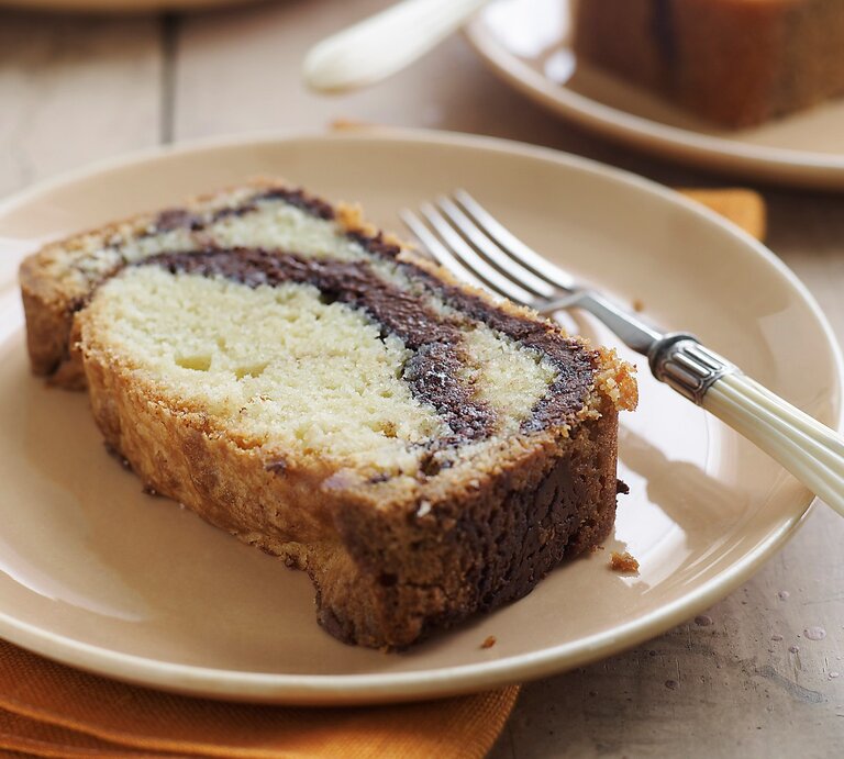Ein heller Tisch mit mehreren weißen Tellern auf dem jeweils ein Stück Marmorkuchen mit Nutella liegt. Am Rand des Tellers eine Gabel mit weißem Griff und darunter eine gelbe Serviette. | © Gettyimages/ Alexandra Grablewski
