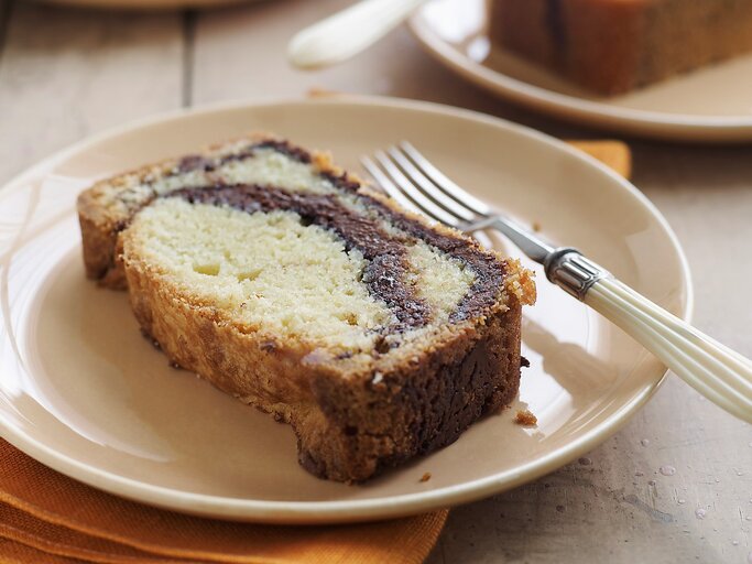 Ein heller Tisch mit mehreren weißen Tellern auf dem jeweils ein Stück Marmorkuchen mit Nutella liegt. Am Rand des Tellers eine Gabel mit weißem Griff und darunter eine gelbe Serviette. | © Gettyimages/ Alexandra Grablewski