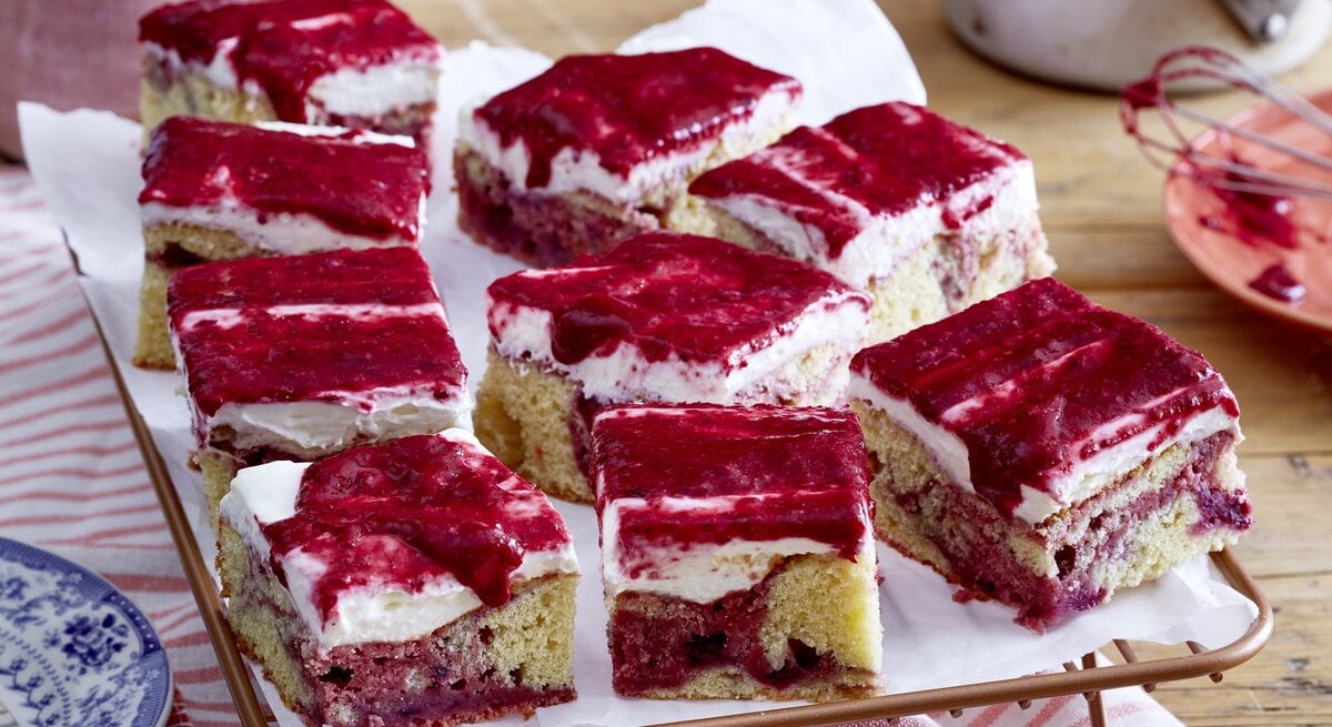 Beeren-Marmorkuchen vom Blech mit cremiger Frischkäseglasur, in Würfel geschnitten auf einem weißen Tuch. 