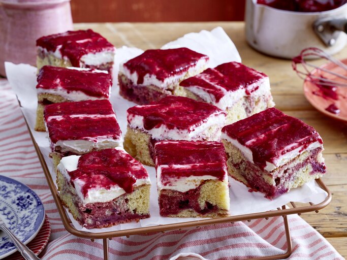 Beeren-Marmorkuchen vom Blech mit cremiger Frischkäseglasur, in Würfel geschnitten auf einem weißen Tuch.  | © EAT CLUB/Isabell Triemer
