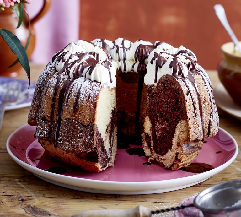 Auf einem Teller liegt ein angeschnittener Baileys-Marmorkuchen. Er ist mit Sahnetüpfeln verziert und mit Schokolade überzogen.  | © EAT CLUB/Isabell Triemer