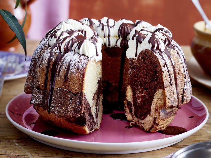 Auf einem Teller liegt ein angeschnittener Baileys-Marmorkuchen. Er ist mit Sahnetüpfeln verziert und mit Schokolade überzogen.  | © EAT CLUB/Isabell Triemer
