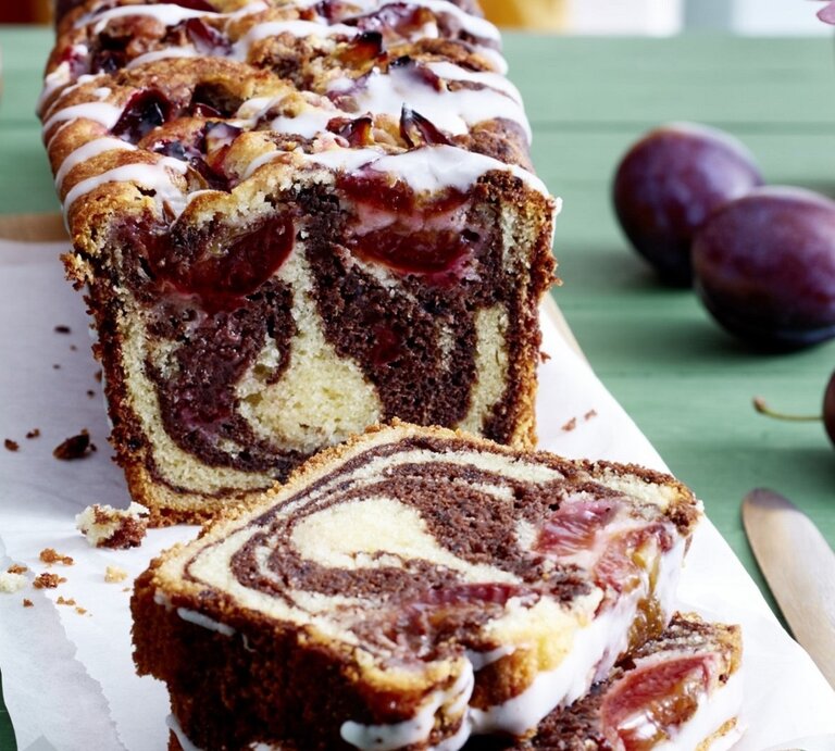 Auf einem Schneidebrett steht ein Zwetschgen Marmorkuchen. Er ist mit Puderzuckerguss überzogen.  | © EAT CLUB / Isabell Triemer
