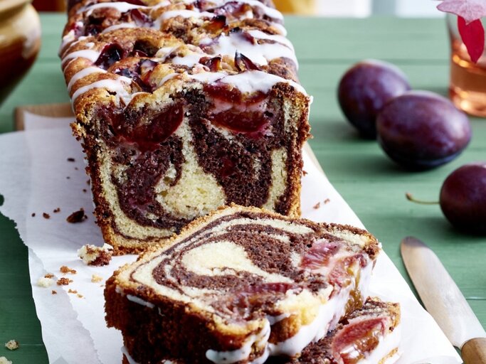 Auf einem Schneidebrett steht ein Zwetschgen Marmorkuchen. Er ist mit Puderzuckerguss überzogen.  | © EAT CLUB / Isabell Triemer
