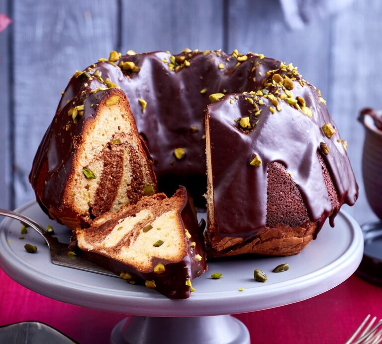 Ein angeschnittener Marmorkuchen auf einer Tortenplatte. Auf dem Tisch ist eine rote Tischdecke und dahinter eine rustikale Holzwand. | © EAT CLUB / Isabell Triemer