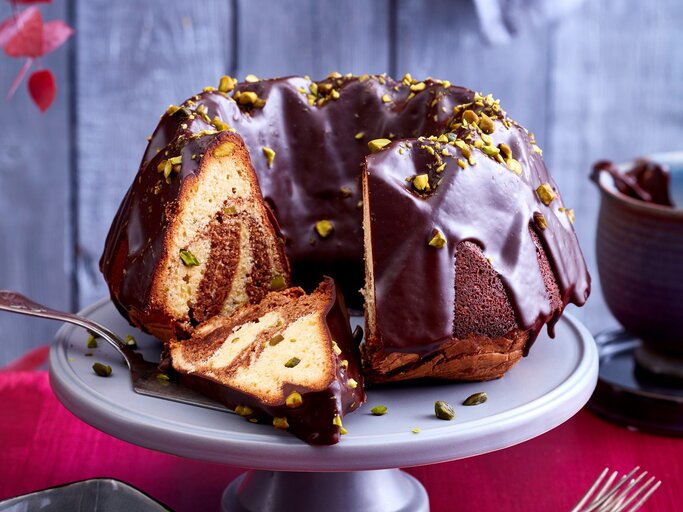 Ein angeschnittener Marmorkuchen auf einer Tortenplatte. Auf dem Tisch ist eine rote Tischdecke und dahinter eine rustikale Holzwand. | © EAT CLUB / Isabell Triemer