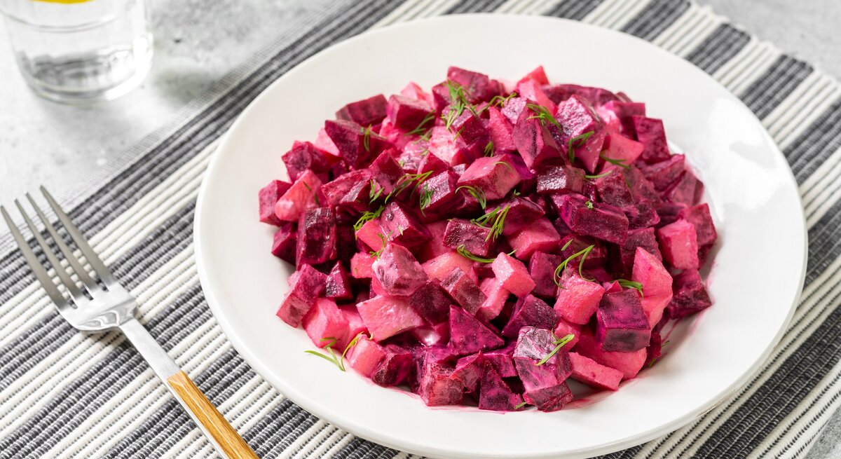 Ein Teller schwedischer Rote-Bete-Salat auf einem Platzdeckchen, daneben eine Gabel und ein Glas.