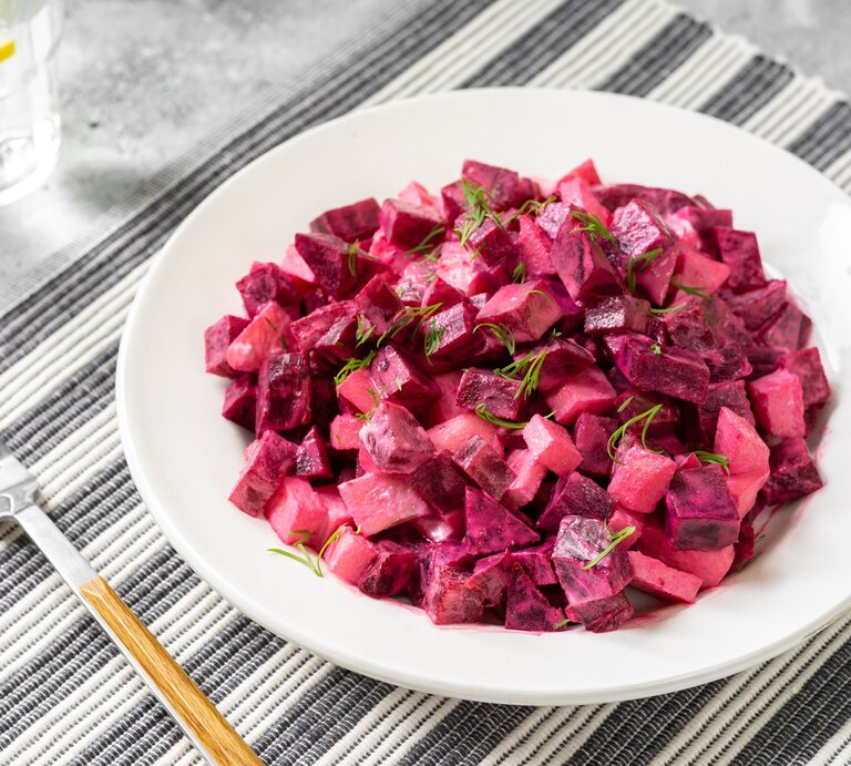 Ein Teller schwedischer Rote-Bete-Salat auf einem Platzdeckchen, daneben eine Gabel und ein Glas. | © Adobe Stock/ klio_l