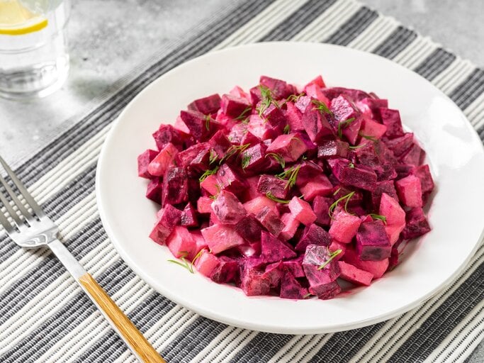 Ein Teller schwedischer Rote-Bete-Salat auf einem Platzdeckchen, daneben eine Gabel und ein Glas. | © Adobe Stock/ klio_l