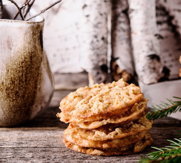 Haferkekse auf einem Holztisch mit einer weißen Vase, Birken und Tanne im Hintergrund. | © Shutterstock/ Trendy Rowdy