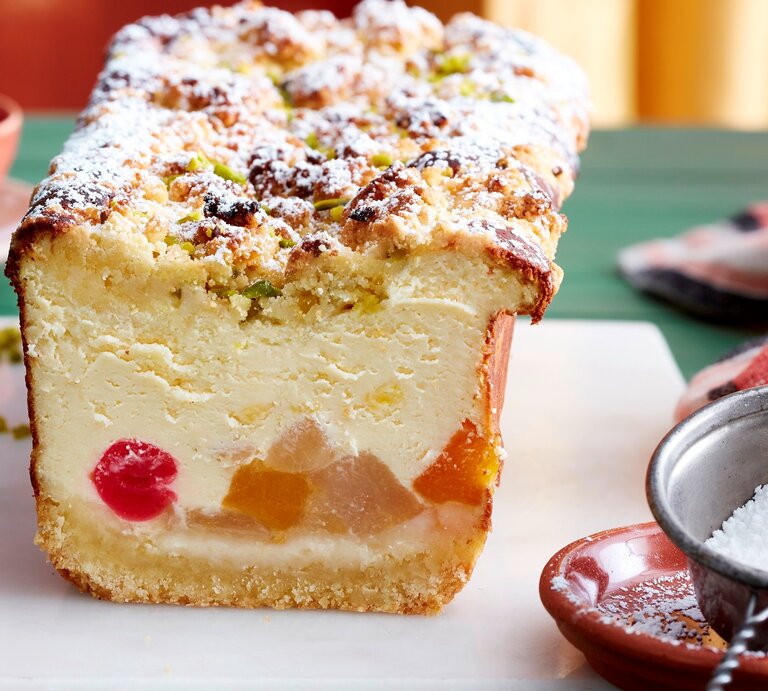 Auf einem Brett steht ein Tutti-Frutti-Käsekuchen aus der Kastenform. Er ist mit Puderzucker bestreut. | © EAT CLUB / Isabell Triemer