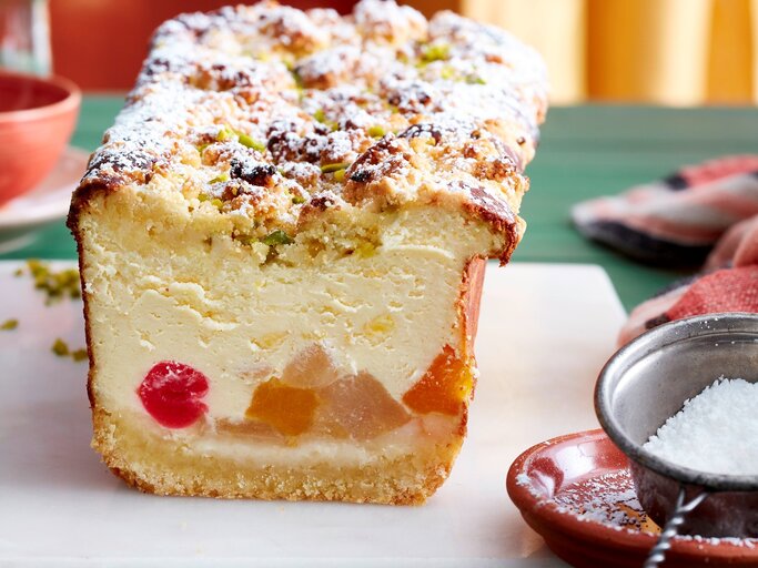Auf einem Brett steht ein Tutti-Frutti-Käsekuchen aus der Kastenform. Er ist mit Puderzucker bestreut. | © EAT CLUB / Isabell Triemer