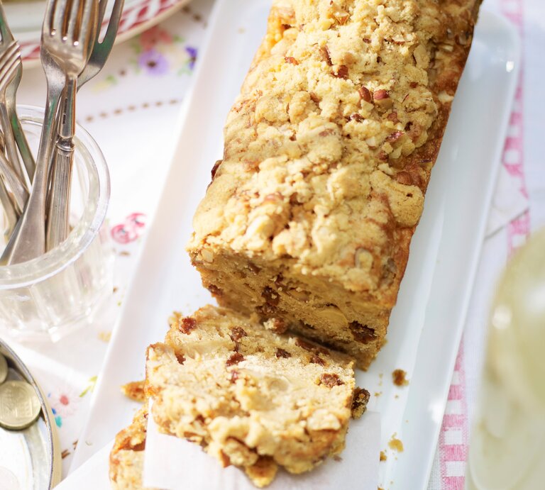 Apfel-Kastenkuchen mit Streuseln angeschnitten und serviert auf einem länglichen weißem Teller und hellem Untergrund. | © StockFood/ Immediate Media/ Good Food