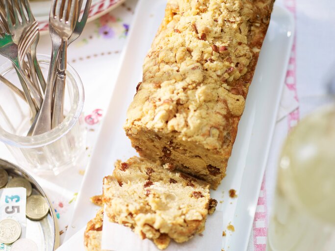 Apfel-Kastenkuchen mit Streuseln angeschnitten und serviert auf einem länglichen weißem Teller und hellem Untergrund. | © StockFood/ Immediate Media/ Good Food