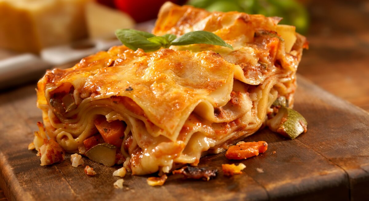 Angeschnittenes Stück Lasagne auf einem Holzbrett. 
