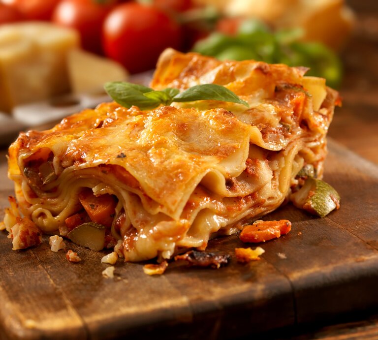 Angeschnittenes Stück Lasagne auf einem Holzbrett.  | © istock/Lauri Patterson