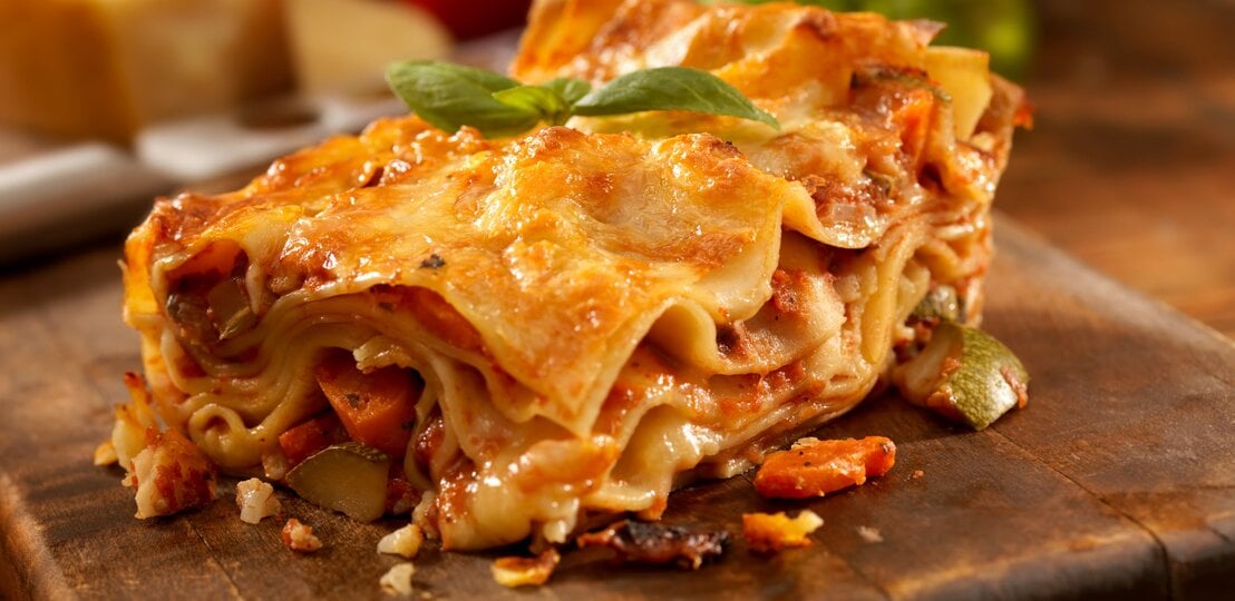 Angeschnittenes Stück Lasagne auf einem Holzbrett.  | © istock/Lauri Patterson