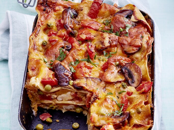 Hähnchen-Lasagne mit Pilzen und frischen Tomaten, angeschnitten in einer großen Auflaufform auf einem weißen Tuch serviert.  | © EAT CLUB / Isabell Triemer