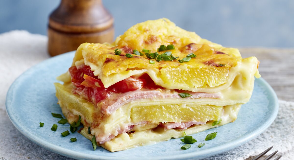 Lasagne Hawaii auf einem blauen Teller auf hölzernem Hintergrund. 