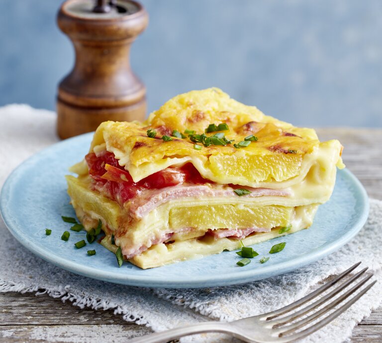 Lasagne Hawaii auf einem blauen Teller auf hölzernem Hintergrund.  | © EAT CLUB/Isabell Triemer