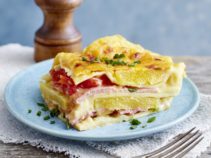 Lasagne Hawaii auf einem blauen Teller auf hölzernem Hintergrund.  | © EAT CLUB/Isabell Triemer