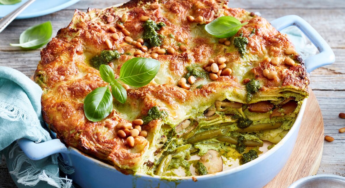 Ein hellblauer Topf mit Pesto-Lasagne auf einem Holzbrett.