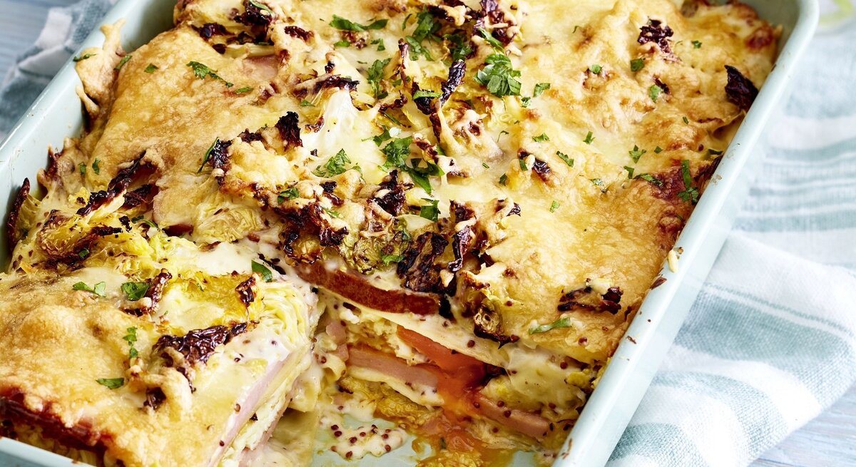 In einer Auflaufform ist eine Fleischkäse-Lasagne mit Wirsingrahm angerichtet. Sie ist mit Kräutern überstreut.