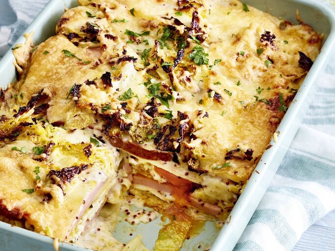 In einer Auflaufform ist eine Fleischkäse-Lasagne mit Wirsingrahm angerichtet. Sie ist mit Kräutern überstreut. | © EAT CLUB / Isabell Triemer