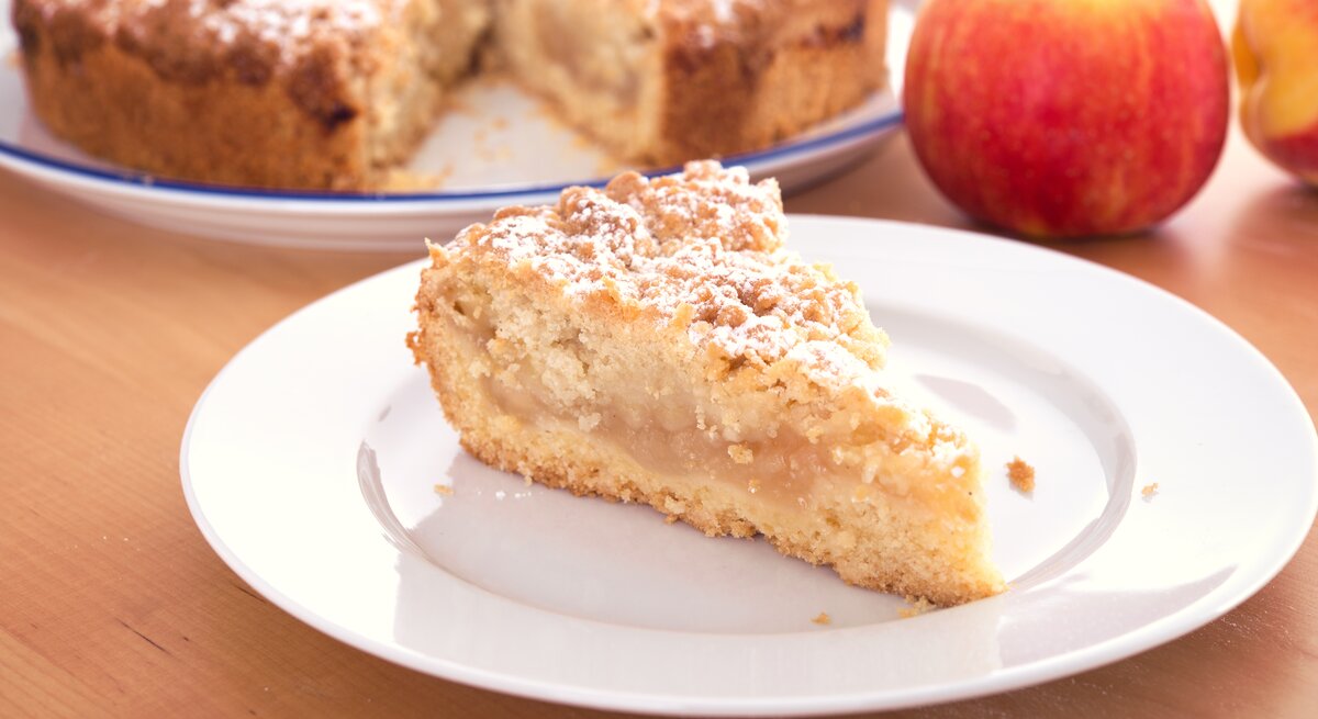 Ein Stück Apfelkuchen mit Streusel auf einem weißen Teller. 