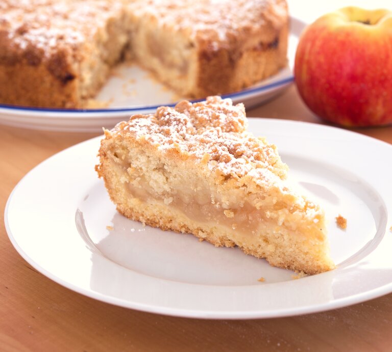 Ein Stück Apfelkuchen mit Streusel auf einem weißen Teller.  | © AdobeStock