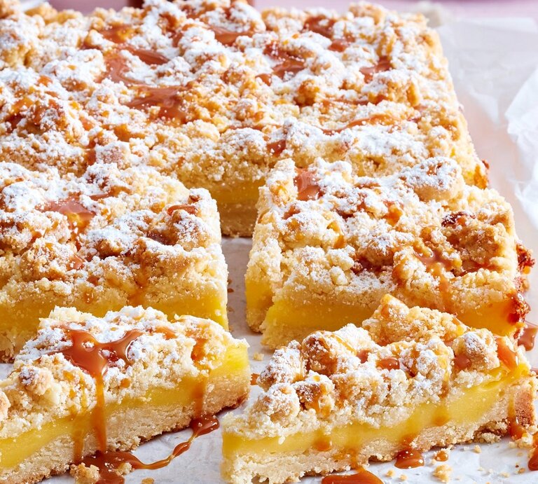 Auf einem Backblech liegt ein Streusel-Puddingkuchen. Er ist bestreut mit Puderzucker und mit Karamellsoße überzogen. Man erkennt die cremige Pudding-Füllung.  | © EAT CLUB/Isabell Triemer