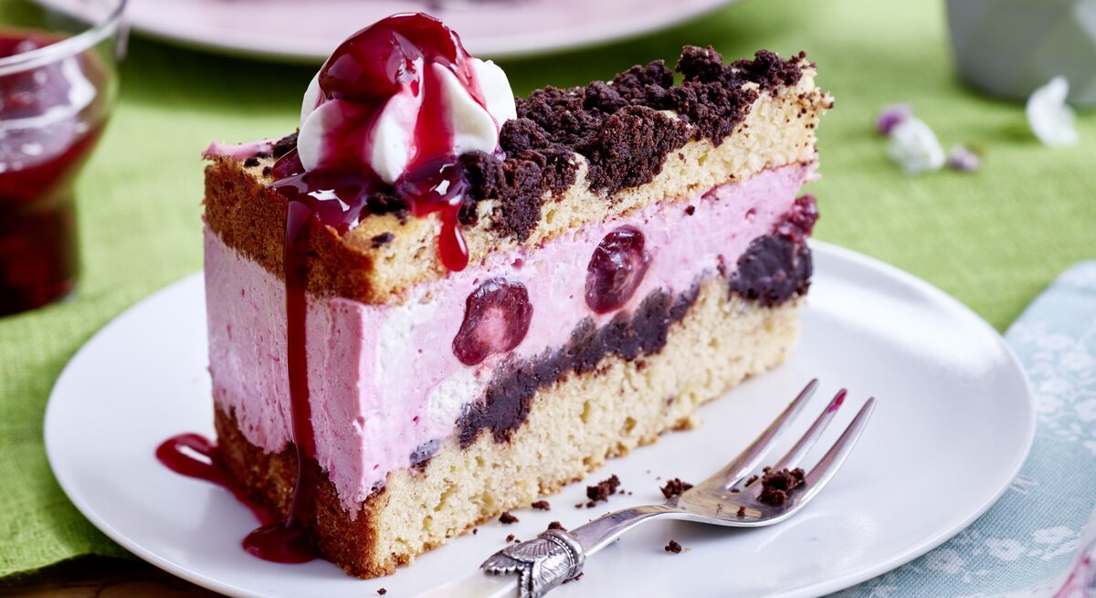 Auf einem Teller steht ein Stück Kiba-Streuseltorte. Es ist mit einem Klecks Schlagsahne verfeinert.
