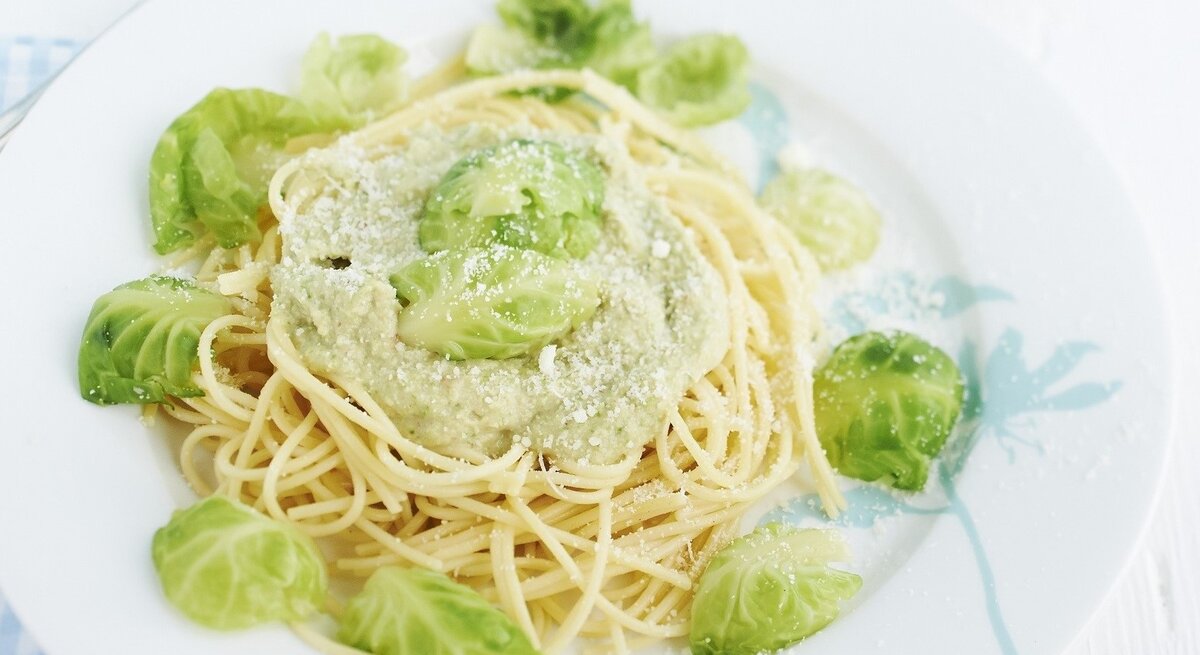 Spaghetti mit Rosenkohlpesto auf weißem Teller und hellem Untergrund. Draufsicht.