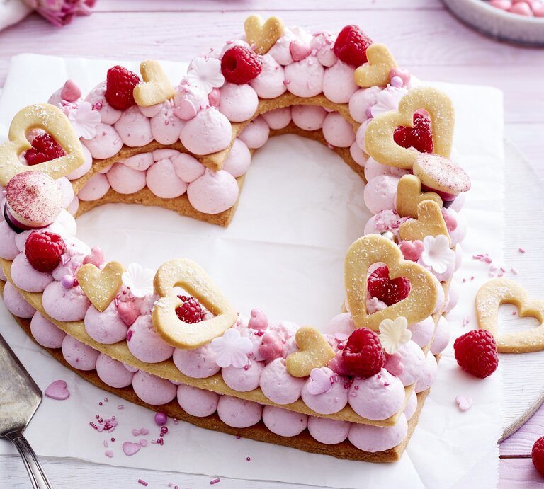 Auf einem Teller liegt ein Herz-Lettercake. Er ist dekoriert mit Zuckerperlen, Keks-Herzen, Himbeeren und rosa Creme.  | © EAT CLUB/Isabell Triemer