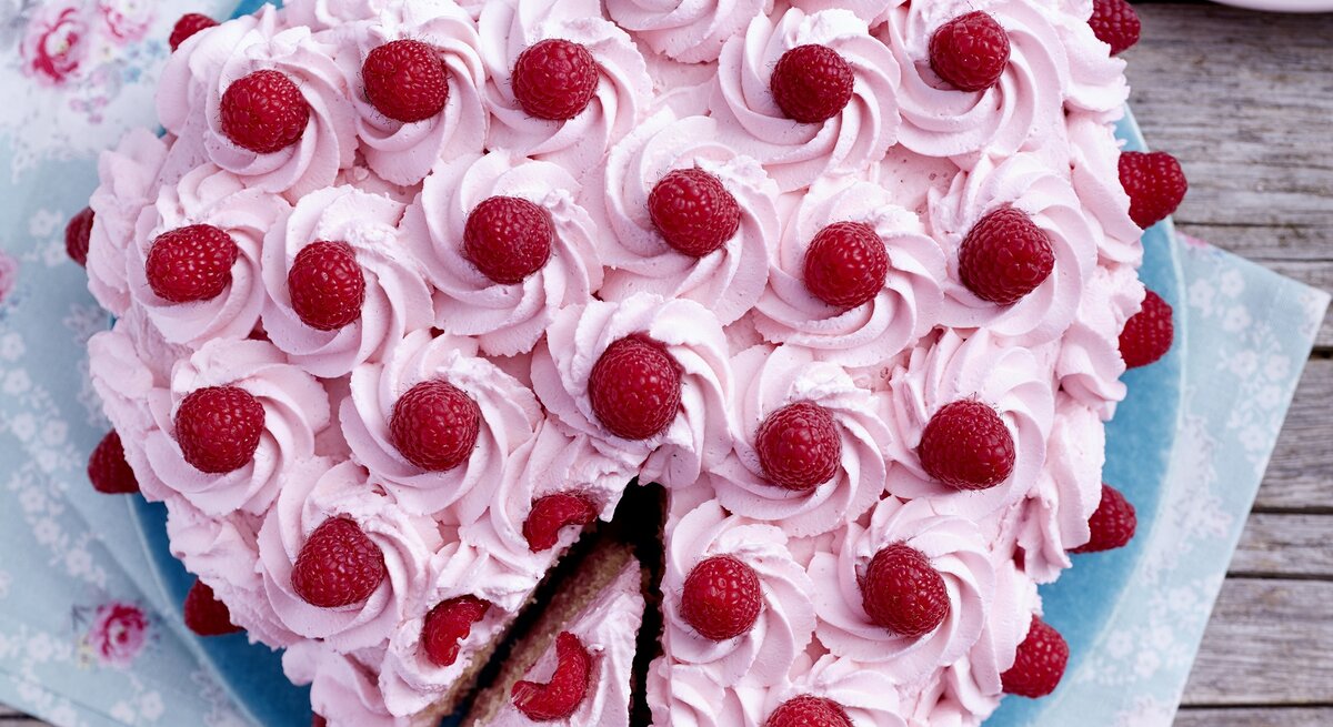Herz-Himbeertorte auf einem blauen Teller auf hölzernem Hintergrund. 