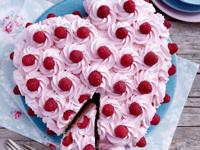 Herz-Himbeertorte auf einem blauen Teller auf hölzernem Hintergrund.  | © EAT CLUB/Isabell Triemer