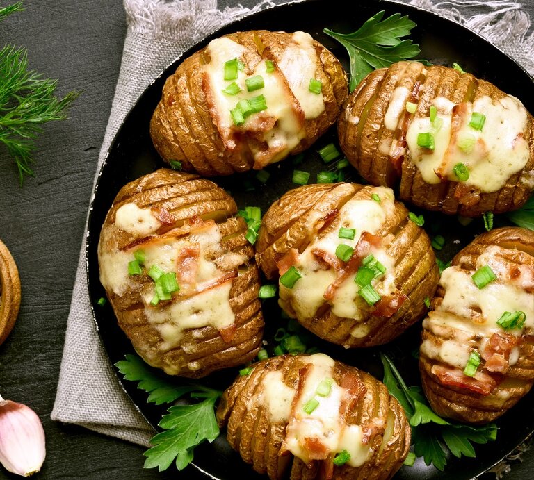 Eine Pfanne mit den Hasselback-Kartoffeln auf einer grauen Decke und einem Schiefer-Untergrund. | © Shutterstock/ Tatiana Volgutova