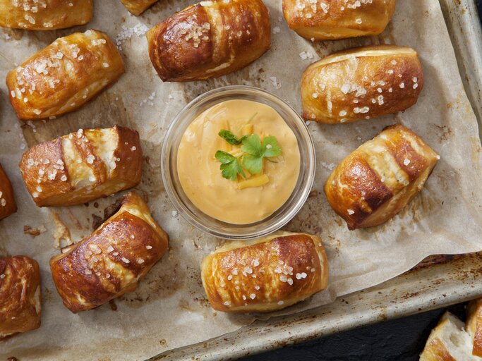 Selbstgemachte Bretzel-Happen auf einem Backblech mit Backpapier neben einer Schüssel mit Käsedip.  | © Getty Images / LauriPatterson