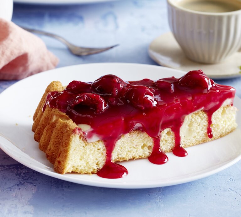 Pudding-Kirschkuchen auf einem weißen Teller, blauer Untergrund und Geschirr und Küchentuch im Hintergrund.  | © EAT CLUB / Isabell Triemer