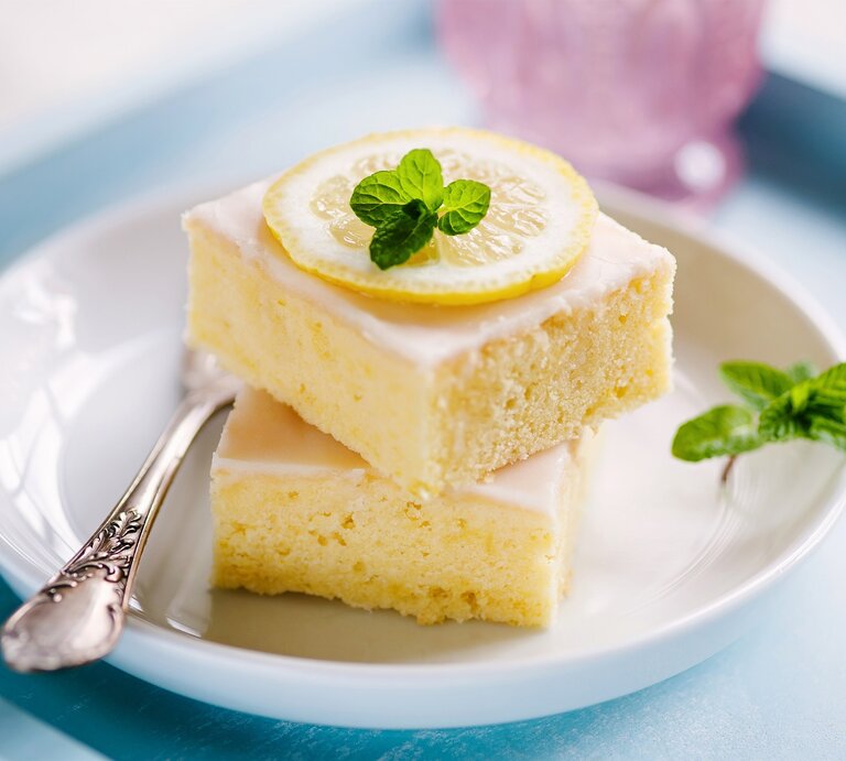 Zwei quadratische Stücke Zitronenkuchen auf einem weißen Teller.  | © Shutterstock/aliasemma