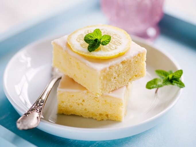 Zwei quadratische Stücke Zitronenkuchen auf einem weißen Teller.  | © Shutterstock/aliasemma