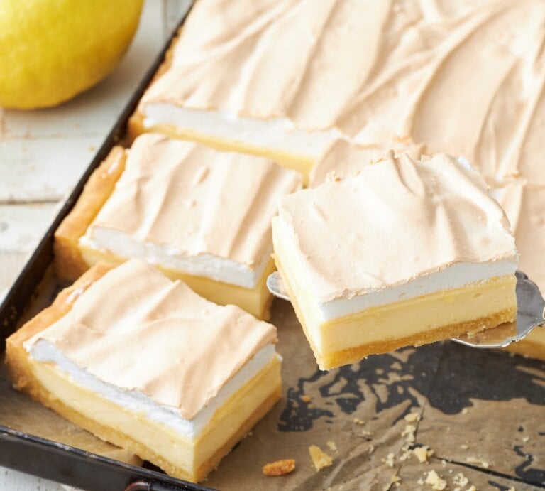 Zitronen-Schmand-Kuchen mit Baiser in einem dunklen Blech auf einem hellen Tisch mit frischen Zitronen.  | © StockFood / StockFood Studios / Brachat, Oliver